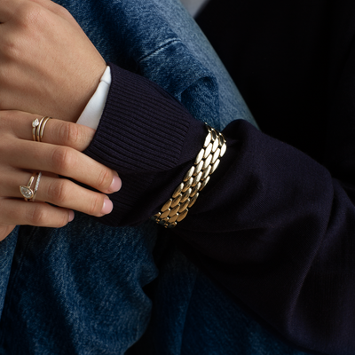 Close-up of a person wearing a gold chain bracelet and multiple rings on a dark background