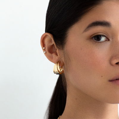 Close-up of a person wearing gold hoop earrings with a plain background