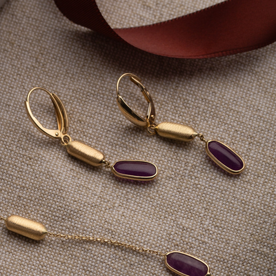 Gold earrings with purple stones on a textured surface