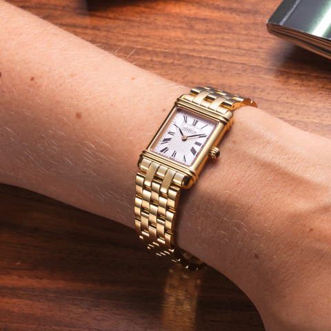 Ladies' Herbelin Art Déco Gold Watch with Roman Numerals on a person's wrist with a wooden surface in the background