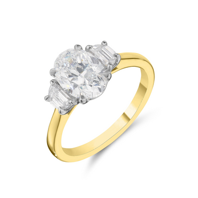 A yellow gold ring with a three-stone diamond cluster setting, featuring a round center diamond and two baguette side diamonds, shown on a clean white background.