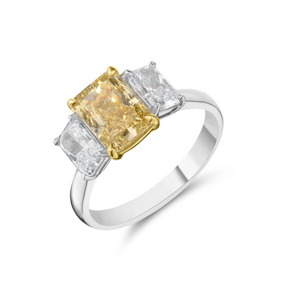 A three-stone diamond ring featuring a central cushion-cut yellow diamond flanked by two round brilliant-cut diamonds, set in a yellow-gold and white gold band with a polished silver-colored shank.