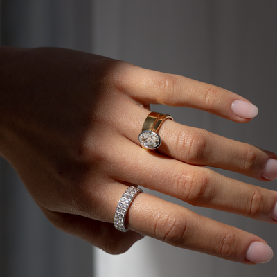 Hand wearing two diamond rings on a neutral background