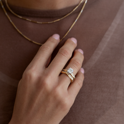 Hand wearing a gold ring with a diamond on a brown background