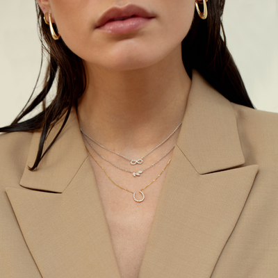 Close-up of a woman wearing gold necklaces and earrings against a neutral background