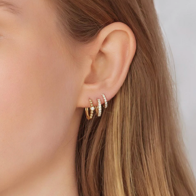Close-up of an ear wearing gold hoop earrings with a blurred background