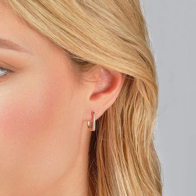 Close-up of a person wearing gold hoop earrings with a neutral background
