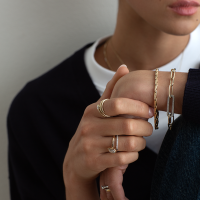 Close-up of a person's hand wearing multiple gold rings and bracelets against a neutral background