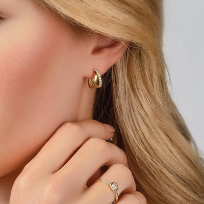 Close-up of a person wearing gold hoop earrings and a ring with a clear stone.