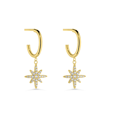 A pair of gold huggie hoop earrings with dangling eight-pointed starburst charms paved with clear stones, shown on a solid white background.
