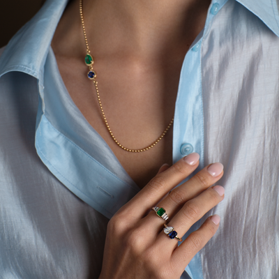 Gold necklace with green and blue gemstones worn by a person in a light blue shirt.