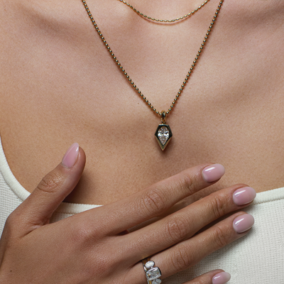 Necklace with a teardrop-shaped pendant worn by a person, with a hand wearing a ring in the foreground.