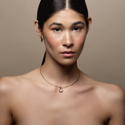 Woman wearing a gold necklace with a pendant against a neutral background