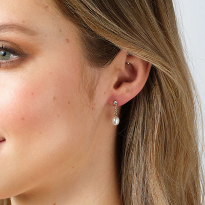 Close-up of a woman wearing pearl earrings with a plain background