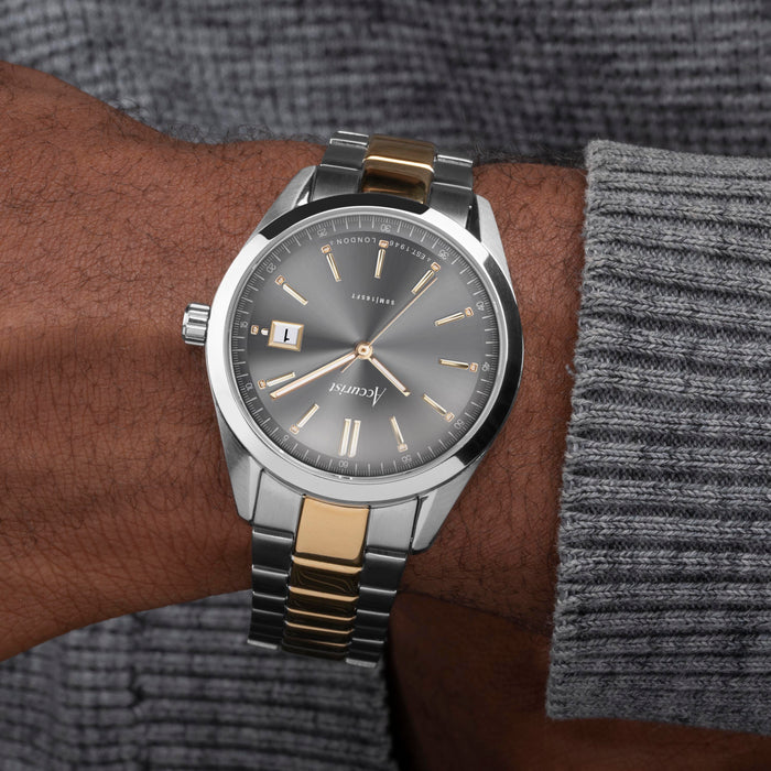 Silver and gold watch on a wrist with a gray sweater sleeve.