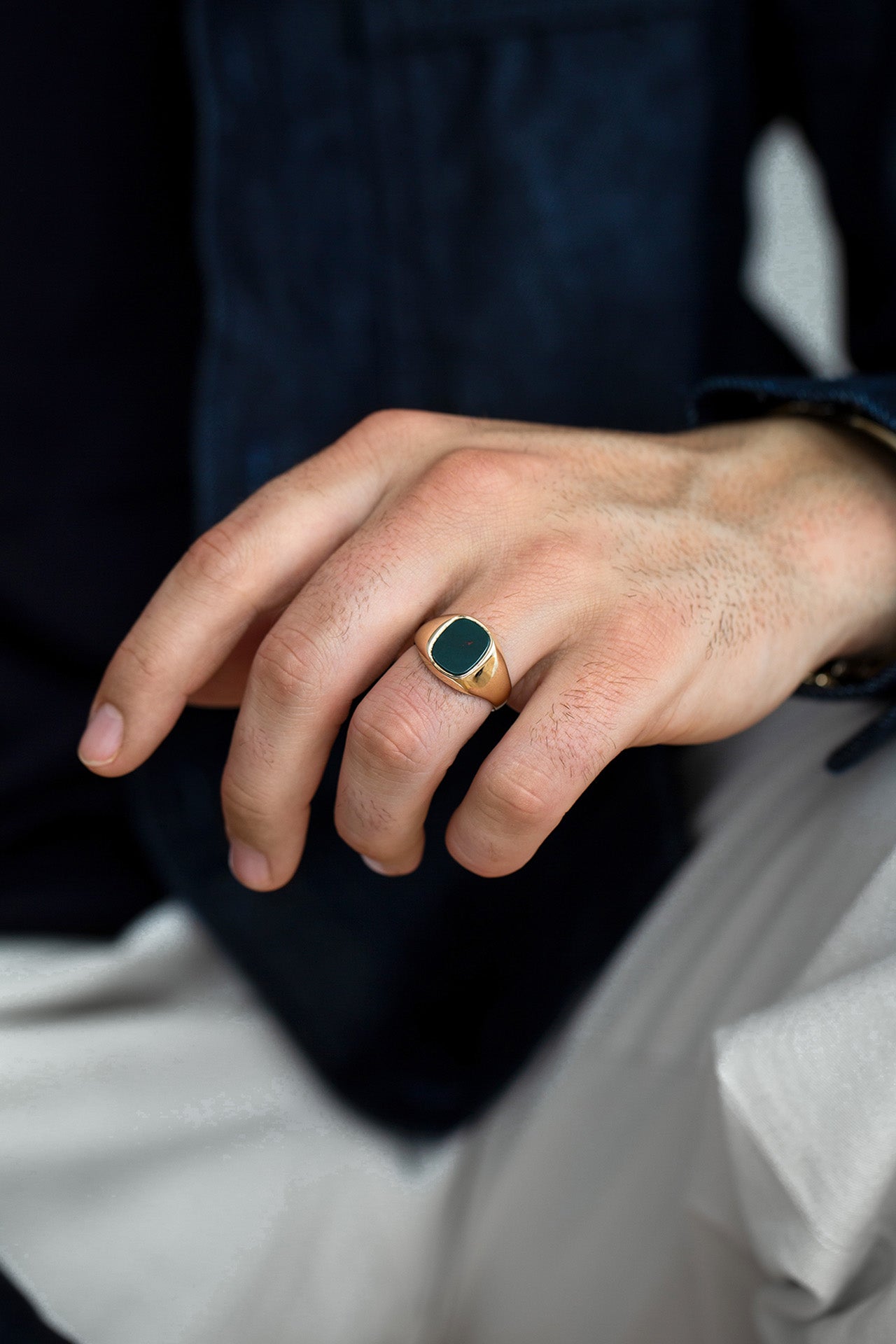 Hand wearing a gold ring with a green gemstone, blurred background