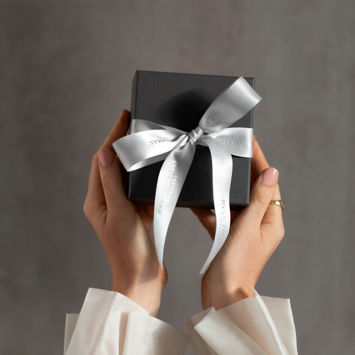 Person holding a black gift box with a white ribbon against a gray background