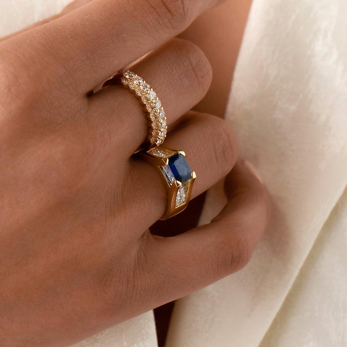 Close-up of a hand wearing two rings with a blue gemstone on a white background