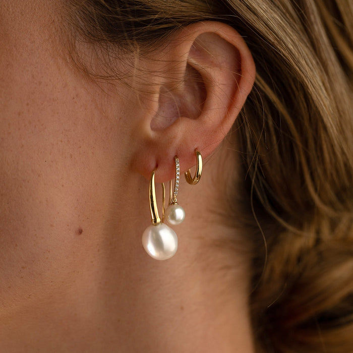 Close-up of an ear wearing gold hoop and pearl earrings.