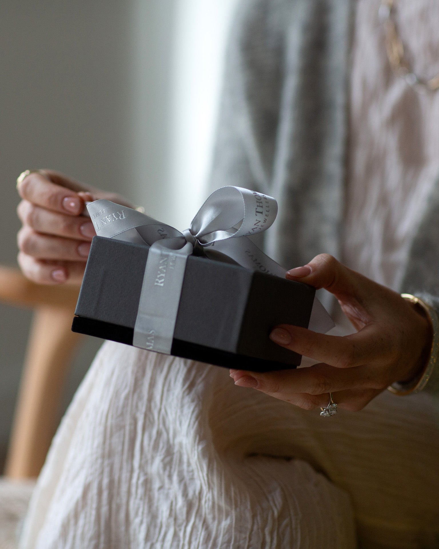 Person holding a small gift box with a ribbon in a softly lit room.