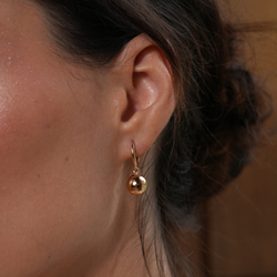 Close-up of a person wearing a gold hoop earring with a blurred background