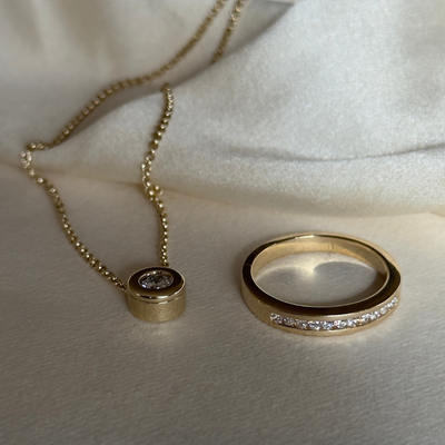 Gold necklace and ring with diamond accents on a white fabric background