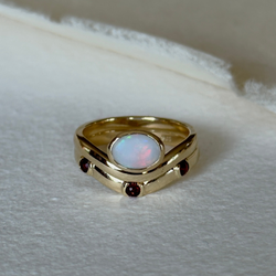 Gold ring with an opal stone and red gemstones on a textured surface
