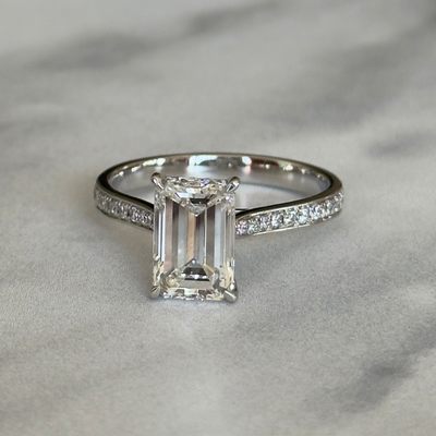 Diamond ring with emerald-cut center stone on a gray background