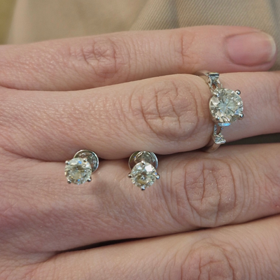 Diamond earrings and ring on a hand against a neutral background