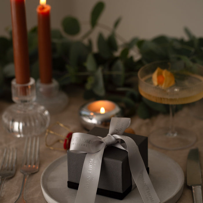 Table setting with a small black gift box, silver ribbon, and lit candles.