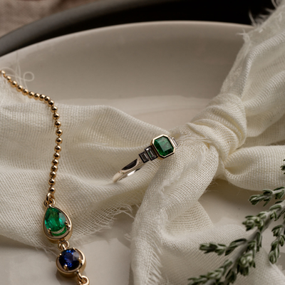 Gold necklace with green gemstones and silver ring on white fabric