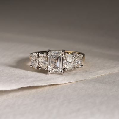 Diamond ring with emerald-cut stones on a textured surface
