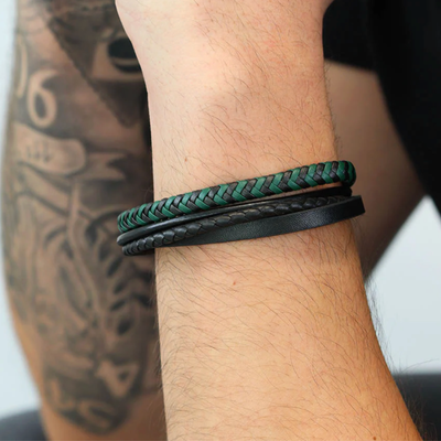 Close-up of a wrist wearing two braided leather bracelets with tattoos on the arm.