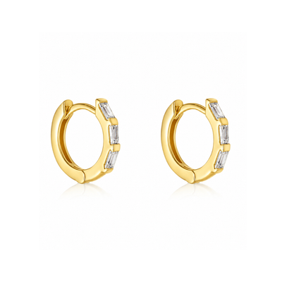 A pair of gold huggie hoop earrings with baguette-cut clear stones, shown on a clean white background with a soft reflection.