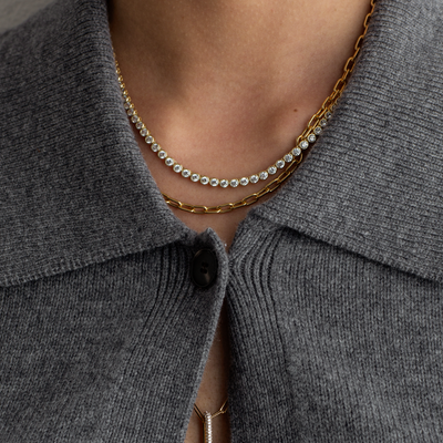Close-up of a person wearing a gold necklace with a gray garment.