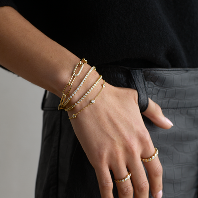 Hand wearing gold bracelets and rings with a black background