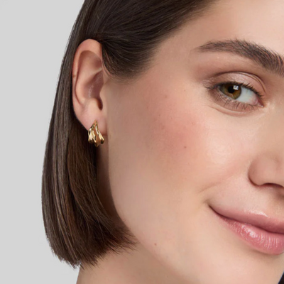 Close-up of a woman wearing a gold earring with a neutral background