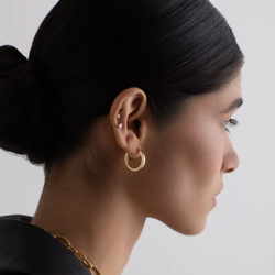 Woman wearing gold hoop earrings with a neutral background