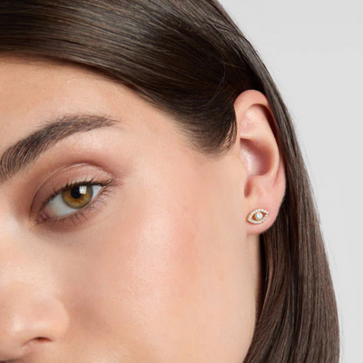 Close-up of a woman wearing a gold earring with a small gemstone on a neutral background