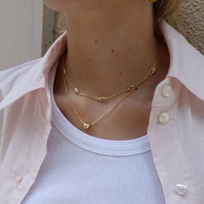 Person wearing a gold necklace with a light pink shirt and white top.