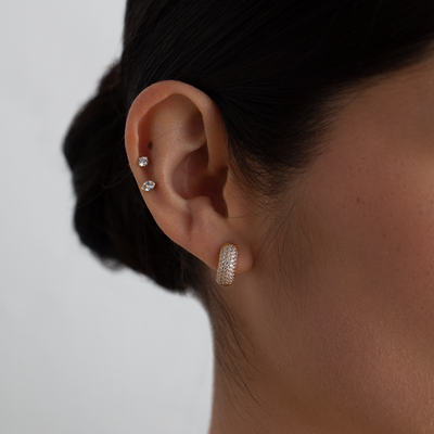 Close-up of an ear wearing two diamond stud earrings and a gold hoop earring on a neutral background.