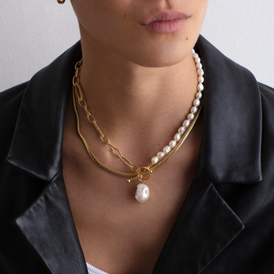 Person wearing a gold chain necklace with pearl pendants against a neutral background