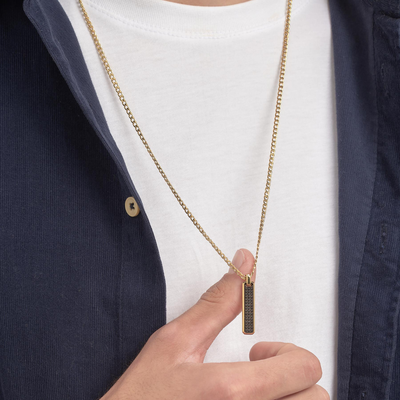 Gold necklace with a pendant held by a hand against a white shirt and navy jacket.