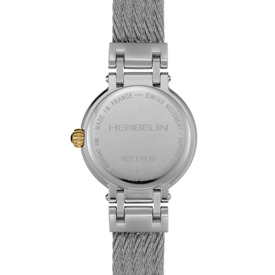 The back of a Herbelin watch with a silver stainless steel case and a textured gray mesh strap, featuring a small gold crown accent.