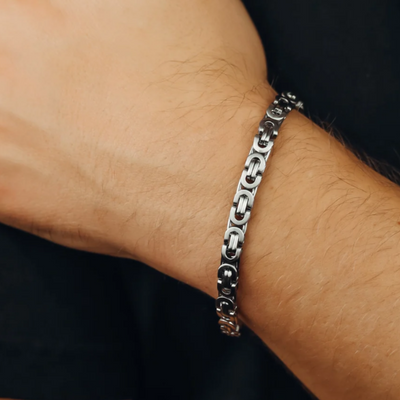 A close-up of a silver-toned metal chain bracelet with interlocking link details worn on a person's wrist against a dark shirt background.