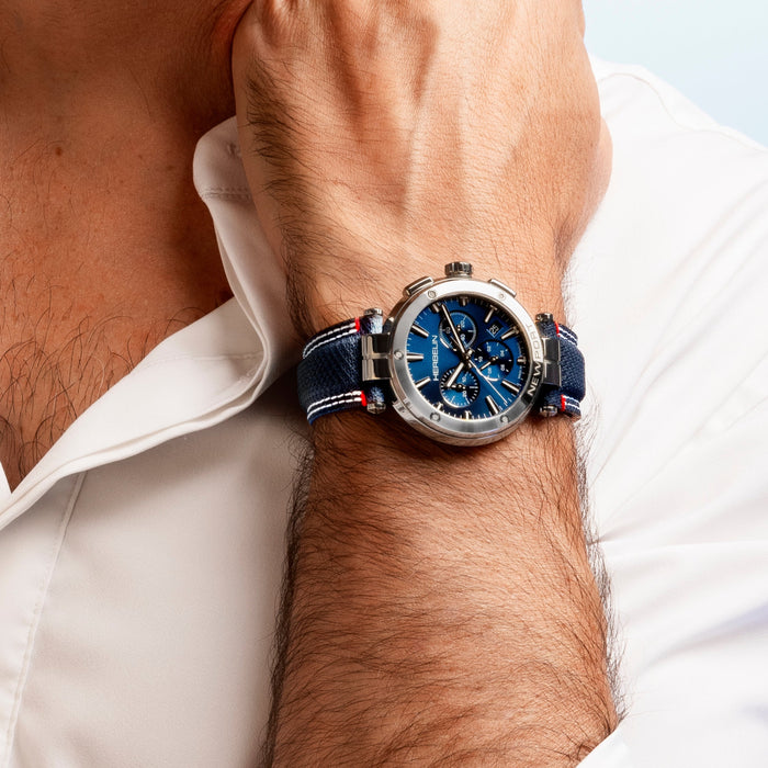 Close-up of a wrist wearing a blue and silver watch with a white shirt background