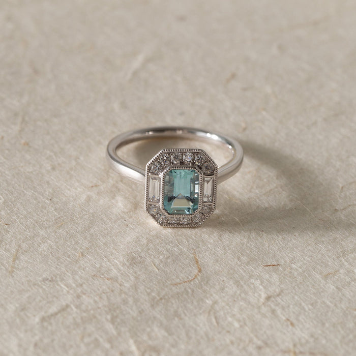 white gold ring with a green gemstone on a textured beige surface