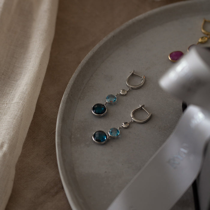 Silver earrings with gemstones on a white plate with a beige cloth background