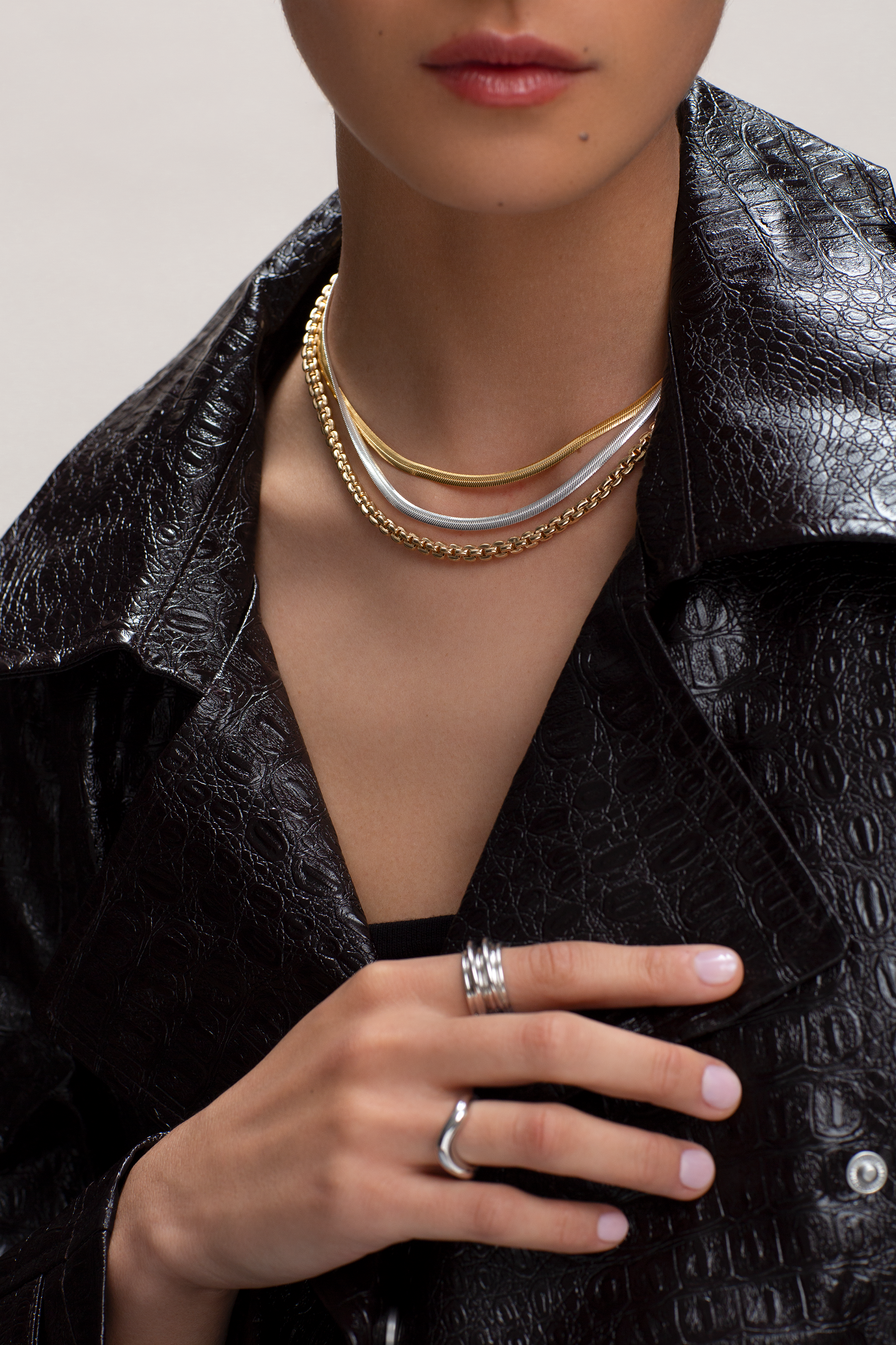 Person wearing gold necklaces and silver rings with a black textured jacket.