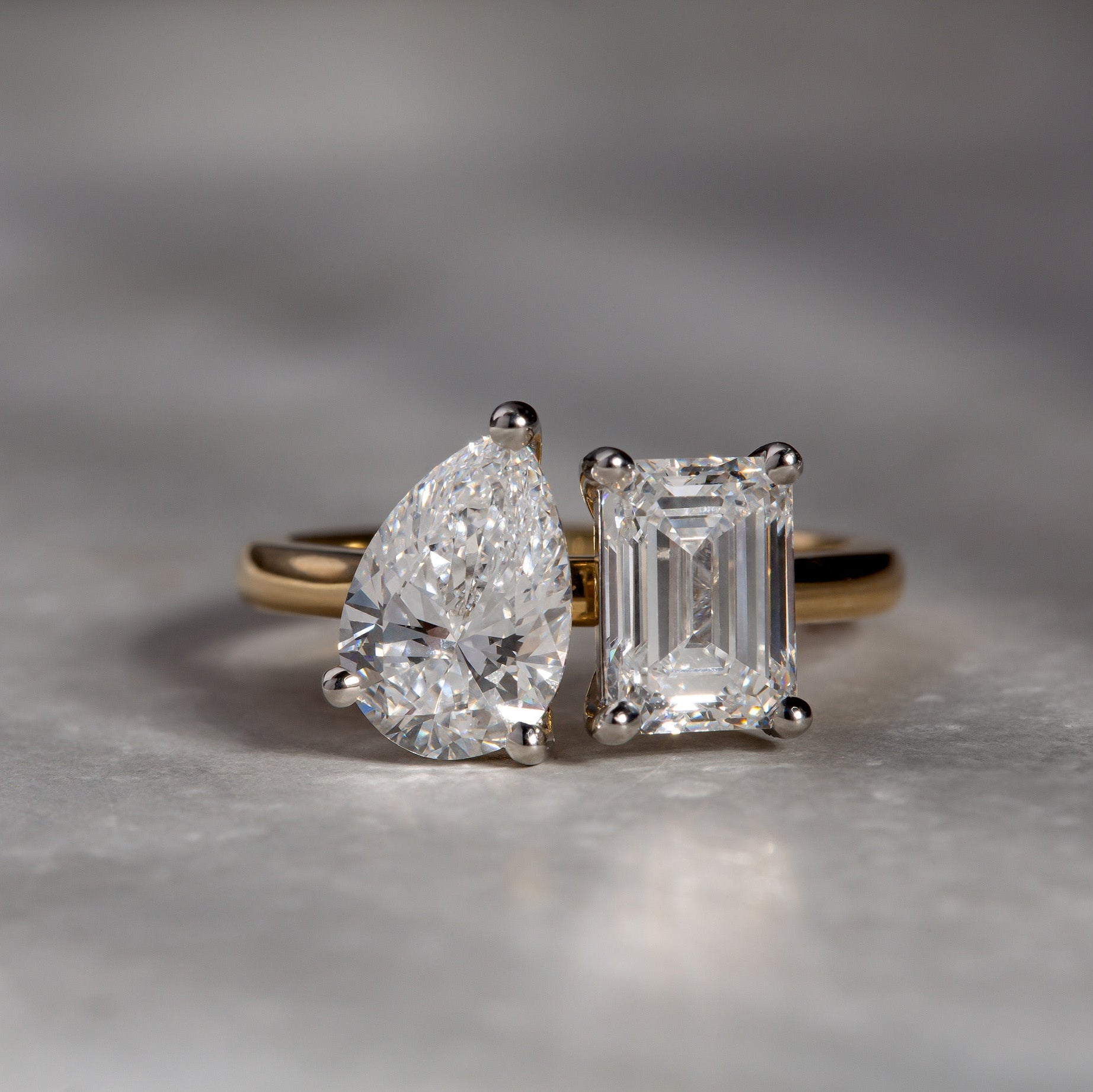 Two diamond rings with pear and emerald cut stones on a gray surface